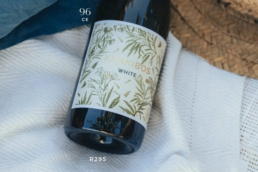 Bottle of Chakibos White wine with botanical label, priced at R295, resting on a white textured cloth.