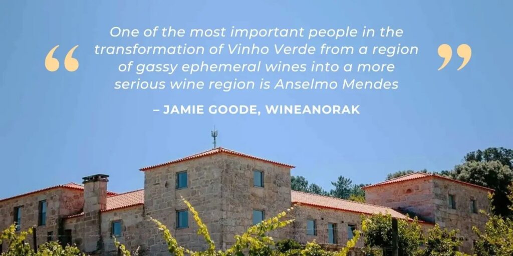 A stone building with red tile roofs is shown under a clear blue sky, accompanied by a quote about Anselmo Mendes and the transformation of the Vinho Verde wine region.