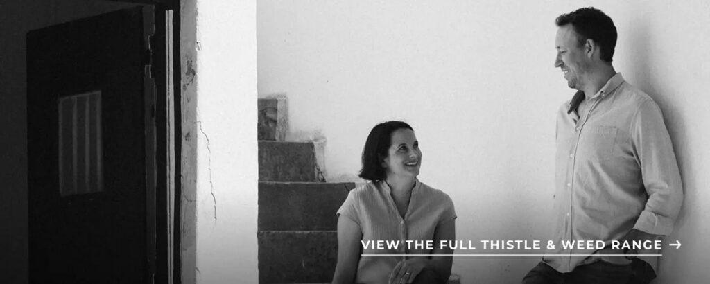 Black-and-white photo of a smiling man and woman indoors, with text: “View the full Thistle & Weed range.”